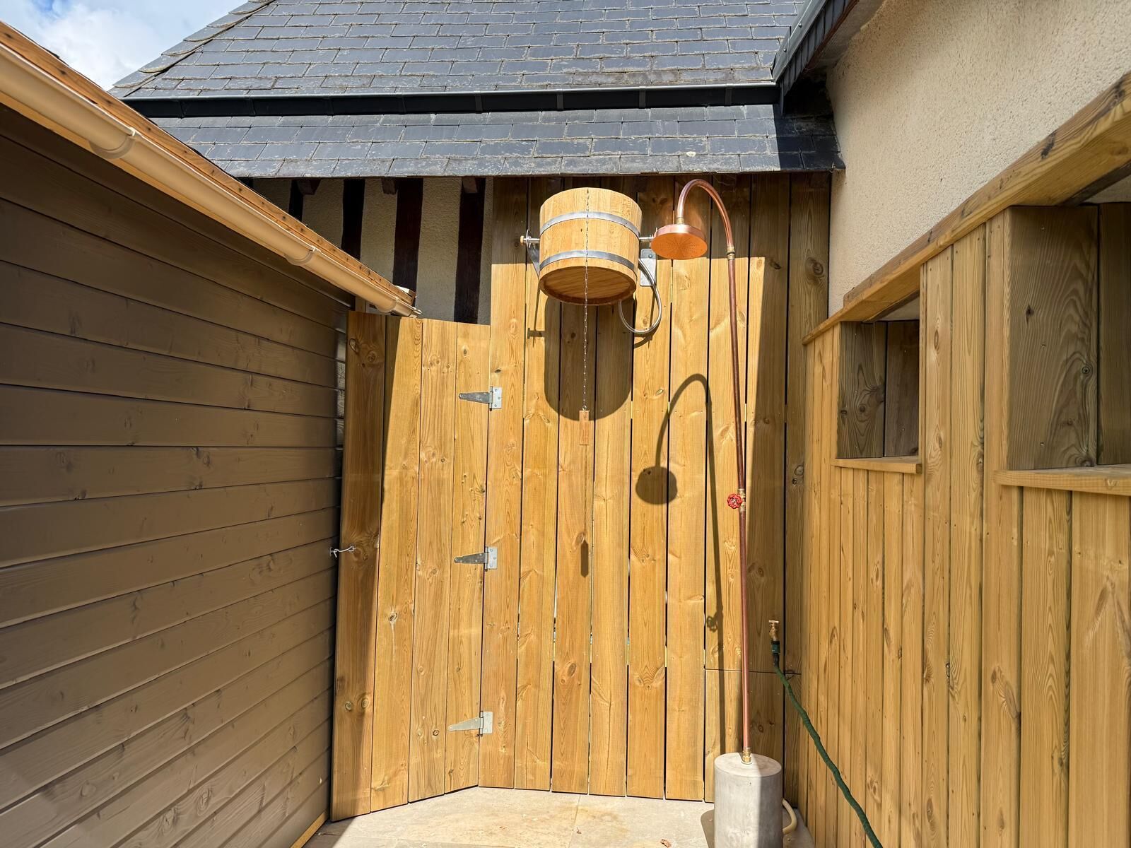 A wooden gate with a metal lock, a wooden barrel, and a hose connected to a metal stand.