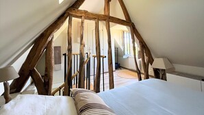 Un dormitorio con techo inclinado, vigas de madera, una cama con almohadas y una mesita de noche.