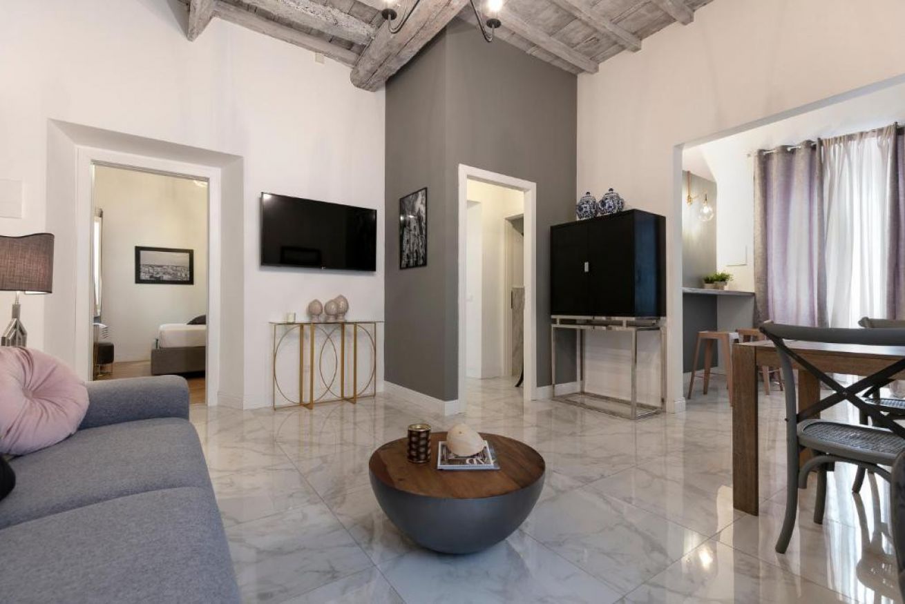 A modern living room with a grey sofa, a coffee table, a flat-screen TV, and a dining area with a table and chairs.
