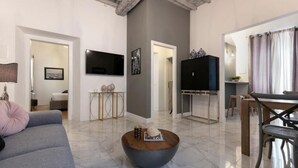 Una sala de estar moderna con un sofá gris, una mesa de centro, un televisor de pantalla plana y un comedor con mesa y sillas.