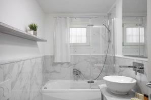 Een moderne badkamer met een badkuip, een douche met glazen wanden, een witte wasbak en een marmeren wand.