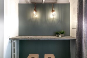 A kitchen with a green backsplash, two pendant lights, a countertop, and two stools. - San Niccolo' Luxury Apartment (Firenze)