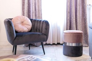 Un soggiorno moderno con una poltrona grigio scuro, un cuscino rosa chiaro e un poggiapiedi nero con dettagli metallici.