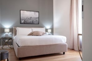 Een slaapkamer met een bed, nachtlampjes, een stadsgezicht in een lijst en een raam met gordijnen.