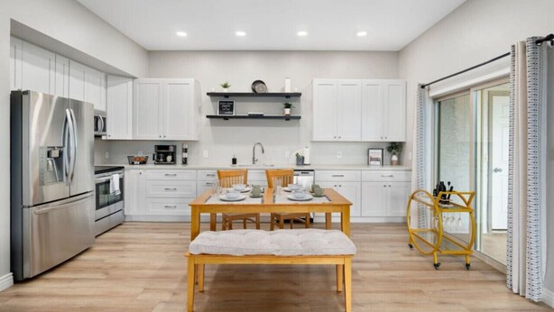 A modern kitchen with white cabinets, a stainless steel refrigerator, a wooden dining table with a bench, and a yellow cart. - Old Town Condo Paradise | Pool | Hot tub | Location (Scottsdale)