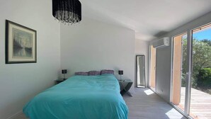 A modern bedroom with a large bed, a chandelier, a framed picture, and a view through large sliding doors.