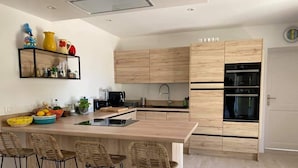 A modern kitchen with a central island, bar stools, wooden cabinets, and a built-in oven.