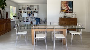 A modern dining area with a glass table and chairs, surrounded by bookshelves and a wooden cabinet.