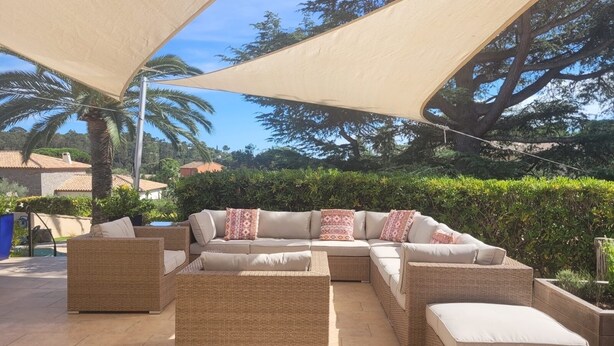 An outdoor seating area with a large woven sofa and ottomans, a table, and a canopy providing shade.