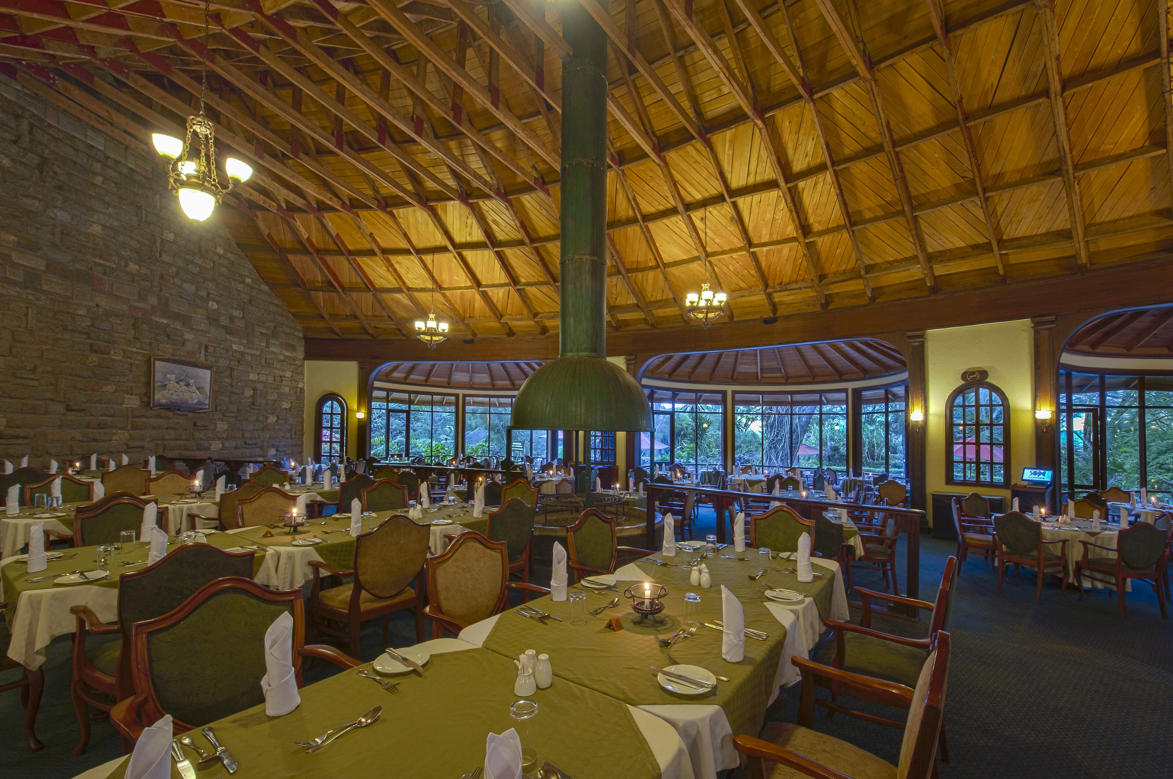 A restaurant with multiple tables set for dining, a brick wall, and large windows offering a view of the outdoors.