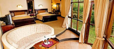 A hotel room with two beds, a sofa, a small table with a bottle and glasses, and a large window with curtains.