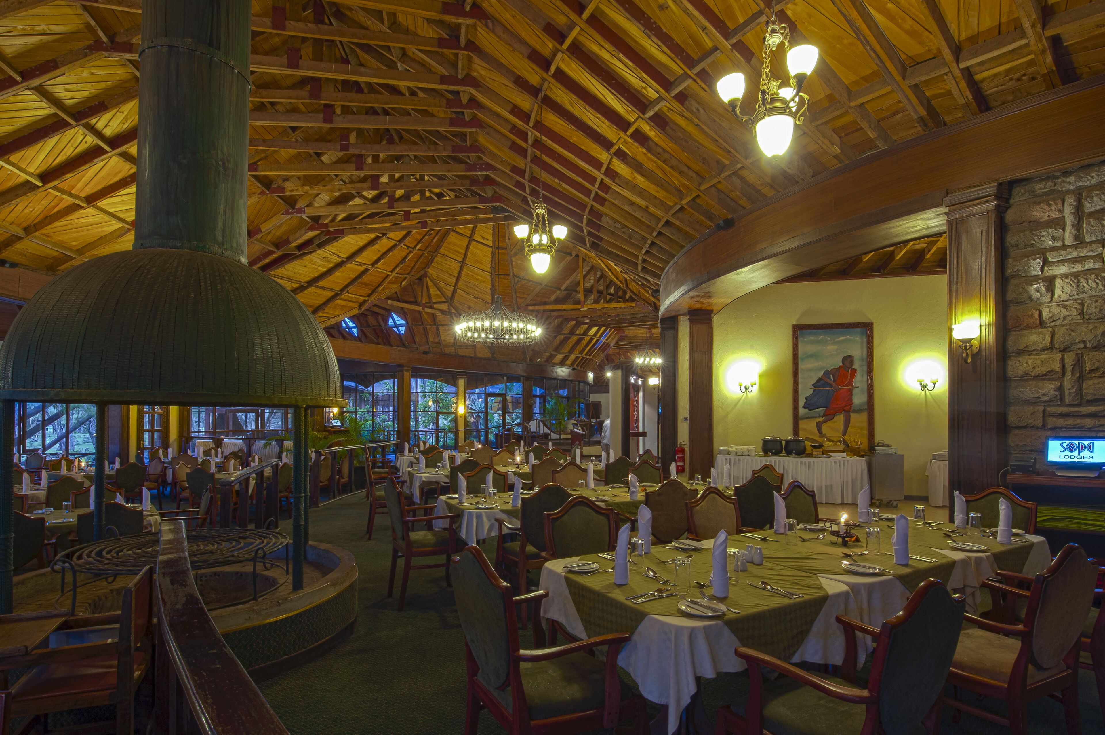 Un restaurante con vigas de madera y candelabros, mesas dispuestas para comer, y una pared de piedra con un cuadro.
