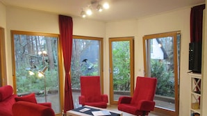 Amplia sala de estar con ventanas grandes, sillas rojas, una mesa de centro y un televisor.