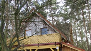 Un edificio rústico de madera con techo amarillo, un banco de madera al frente y un sendero pavimentado.