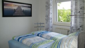 Ein Schlafzimmer mit Bett, einem Fenster mit Vorhängen, einem Heizkörper und einem Bild an der Wand.