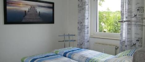 A bedroom with a bed, a window with curtains, a radiator, and a picture on the wall.