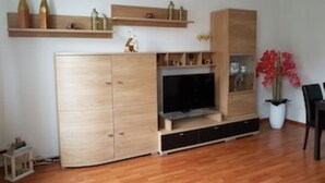 Ein Wohnzimmer mit einem Holzschrank, einem Flachbildfernseher und einer Topfpflanze.