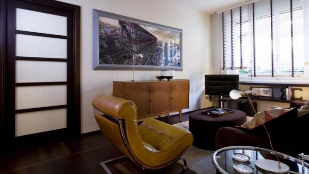 A modern living room with a brown leather armchair, a wooden cabinet, and a large abstract painting on the wall. - Luxury apartment in Ponte Vecchio (Firenze)