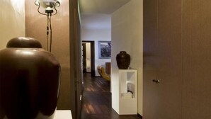 A hallway with a modern lamp, a large vase on a white shelf, and a door leading to another room.