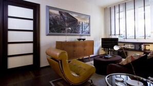 A modern living room with a brown leather armchair, a wooden cabinet, and a large abstract painting on the wall.
