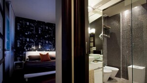 A bedroom with a cityscape wallpaper, a bed, and a nightstand. Adjacent is a bathroom with a glass shower enclosure, a sink, and a toilet. - Luxury apartment in Ponte Vecchio (Firenze)