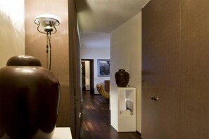 A hallway with a modern lamp, a large vase on a white shelf, and a door leading to another room.