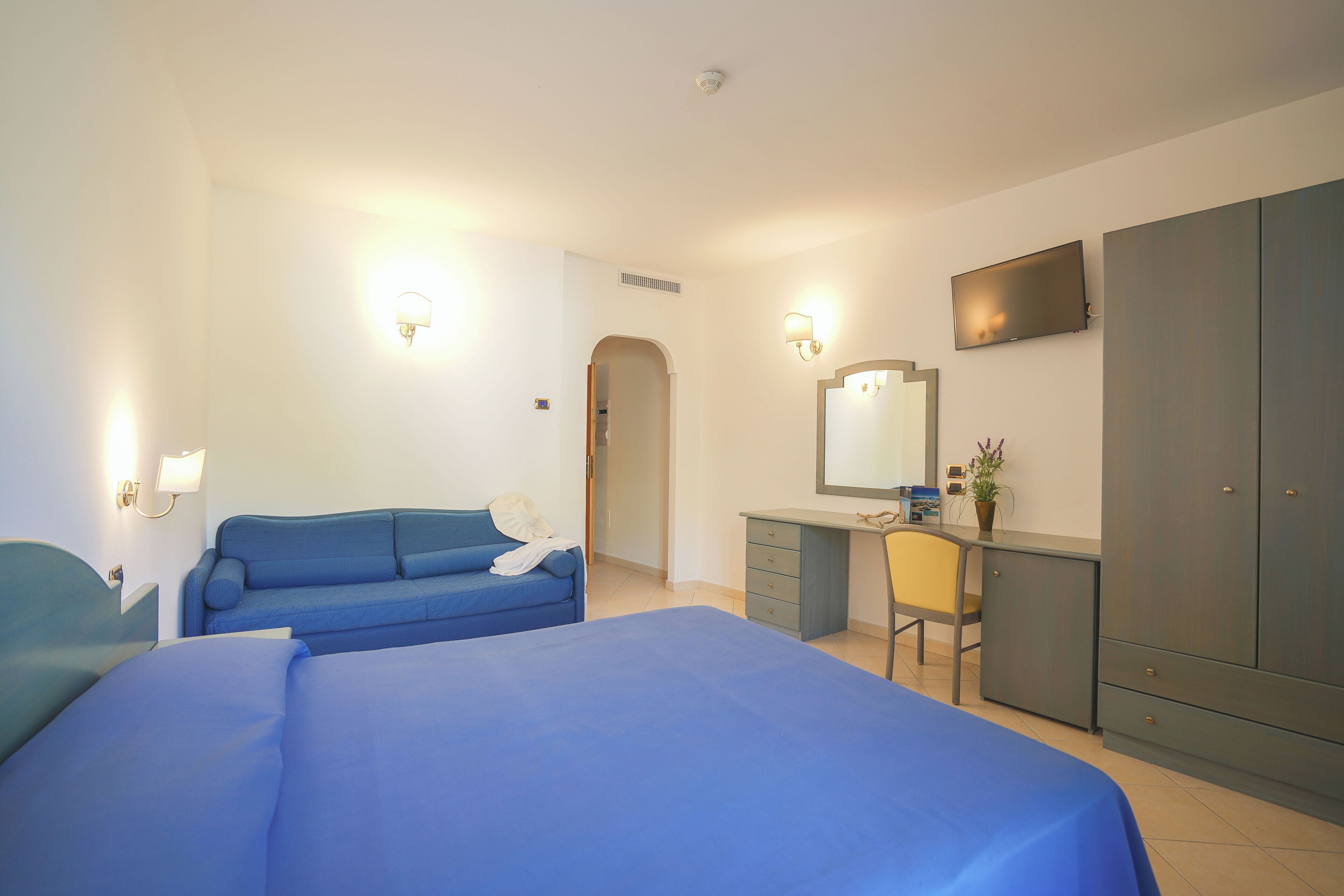 A hotel room with two beds, a desk, a chair, a wardrobe, and a television.