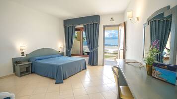 Habitación de hotel con cama, mesita de noche, lámpara, silla y vista al mar.