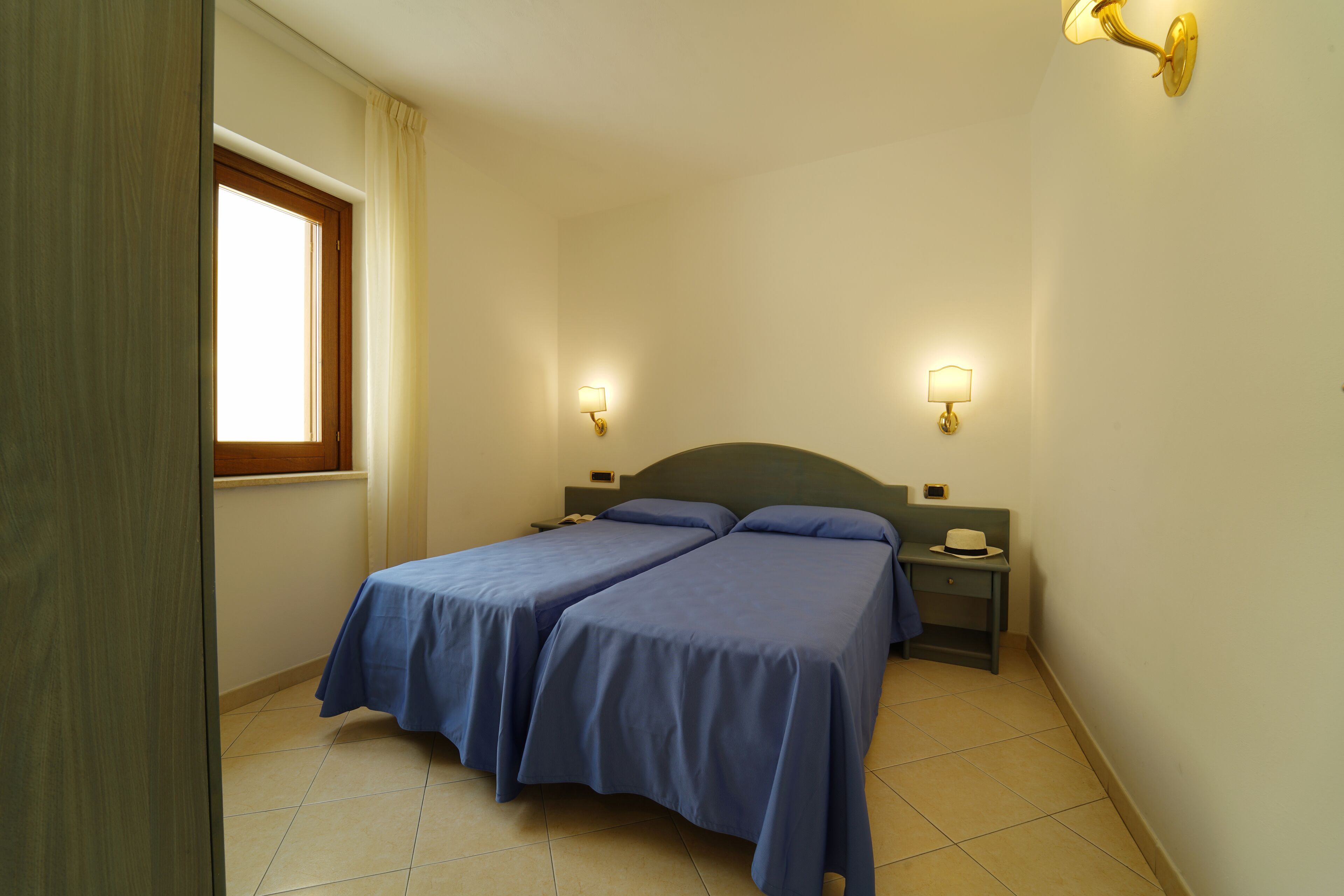 A bedroom with two beds, a window, and two bedside tables with lamps.