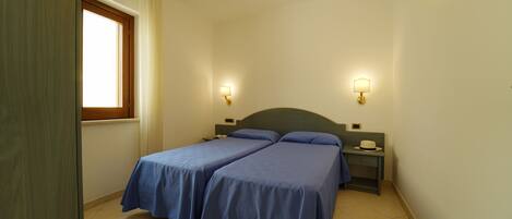 A bedroom with two beds, a window, and two bedside tables with lamps.