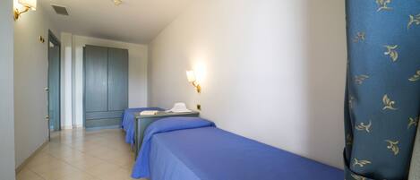 Habitación de hotel con dos camas individuales, un escritorio y una silla. Se ve una puerta que da a otra habitación y una cortina con estampado de hojas.