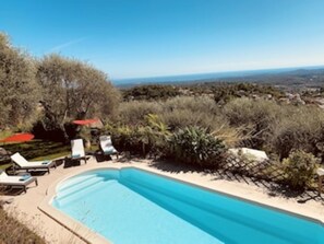 A swimming pool with lounge chairs and umbrellas, surrounded by vegetation and overlooking a distant landscape.