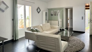 A modern living room with a white sofa, a glass coffee table, and a large window with curtains. - Villa & Spa Mas des Oliviers: Heated pool, sauna, steam room, hot tub, panoramic view (Châteauneuf-Grasse)