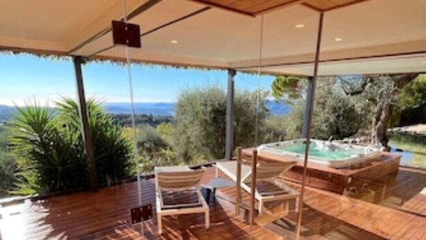 A wooden deck with a glass enclosure, outdoor seating, and a view of the landscape. - Villa & Spa Mas des Oliviers: Heated pool, sauna, steam room, hot tub, panoramic view (Châteauneuf-Grasse)