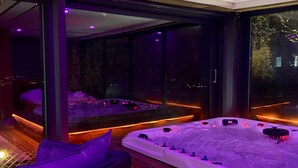A modern spa area with a hot tub, wooden flooring, and a view of the city at night. - Villa & Spa Mas des Oliviers: Heated pool, sauna, steam room, hot tub, panoramic view (Châteauneuf-Grasse)