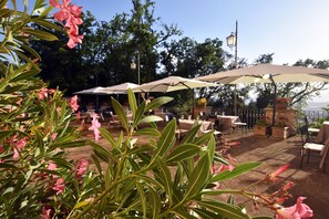 Un espace extérieur aménagé en terrasse, avec des tables et des parasols, entouré de verdure et d’arbres.