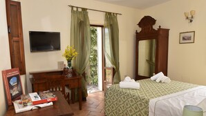 A hotel room with a bed, a desk with a book and a vase of flowers, a TV mounted on the wall, and a balcony with a view. - Agriturismo Villino Bellavista (Spoleto)