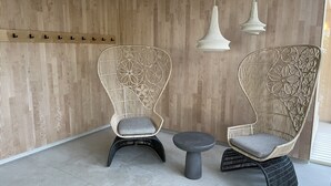 Deux fauteuils en osier avec des coussins, une petite table ronde et un mur composé de lattes de bois verticales, ainsi qu’un luminaire suspendu.
