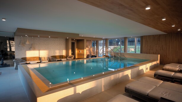 Une grande piscine intérieure dotée d’espaces de détente et offrant une vue sur l’extérieur.