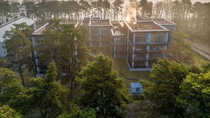 Un bâtiment moderne à plusieurs étages, doté d’un toit plat, entouré d’arbres denses et avec une étendue d’eau en arrière-plan.