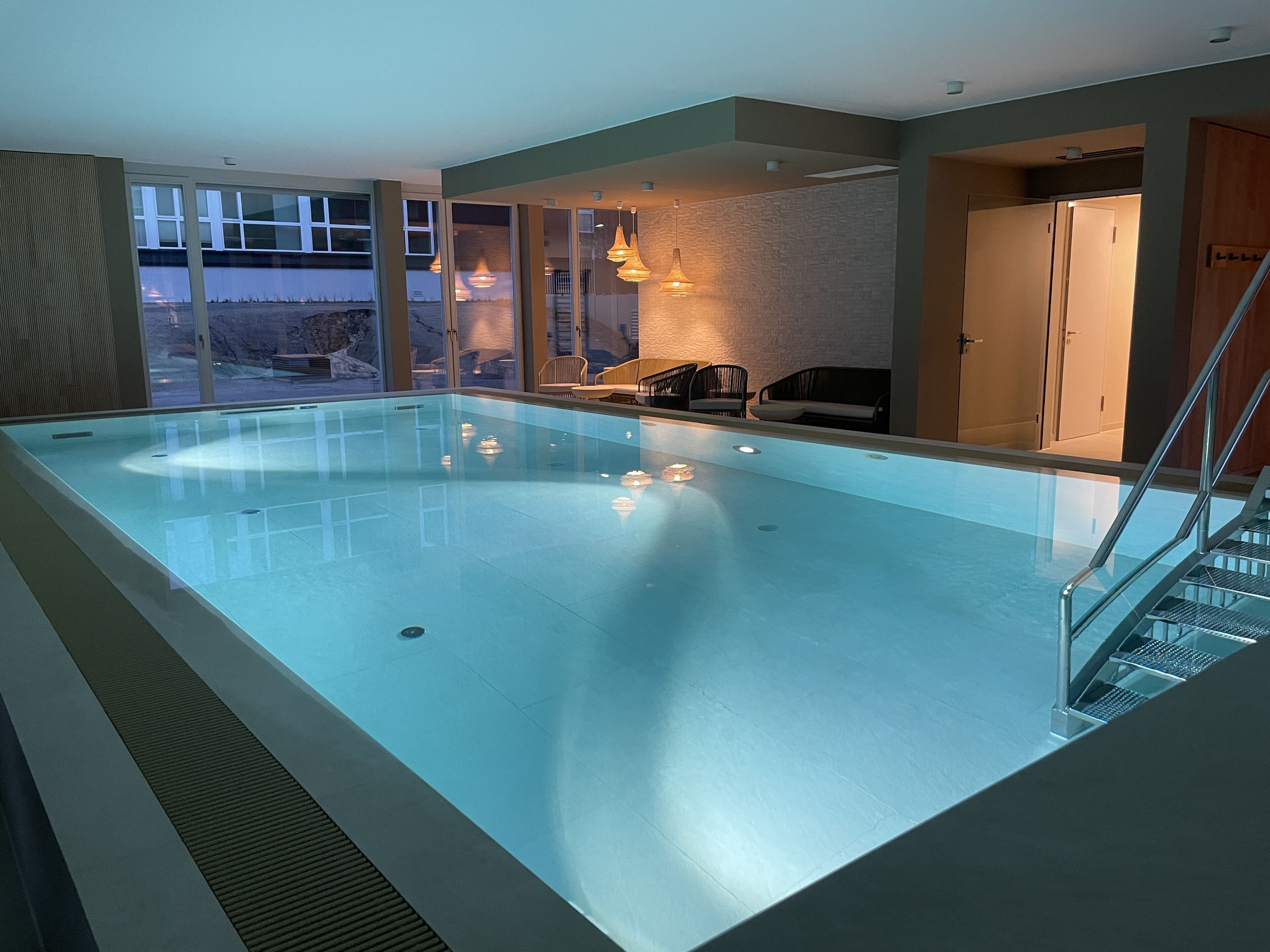 Una piscina interna con vista chiara sull'esterno, un'area relax con sedute e una scala che conduce a un altro piano.