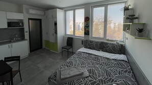 A compact bedroom with a bed, a chair, a desk, and a kitchenette. - DORM BG (Stara Zagora)