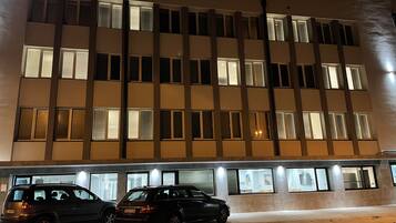 Un edificio de varios pisos con una cuadrícula de ventanas y un estacionamiento con dos automóviles.
