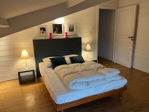 Une chambre à coucher avec un lit, deux lampes de chevet, une tête de lit ornée de tableaux encadrés et un plancher en bois.