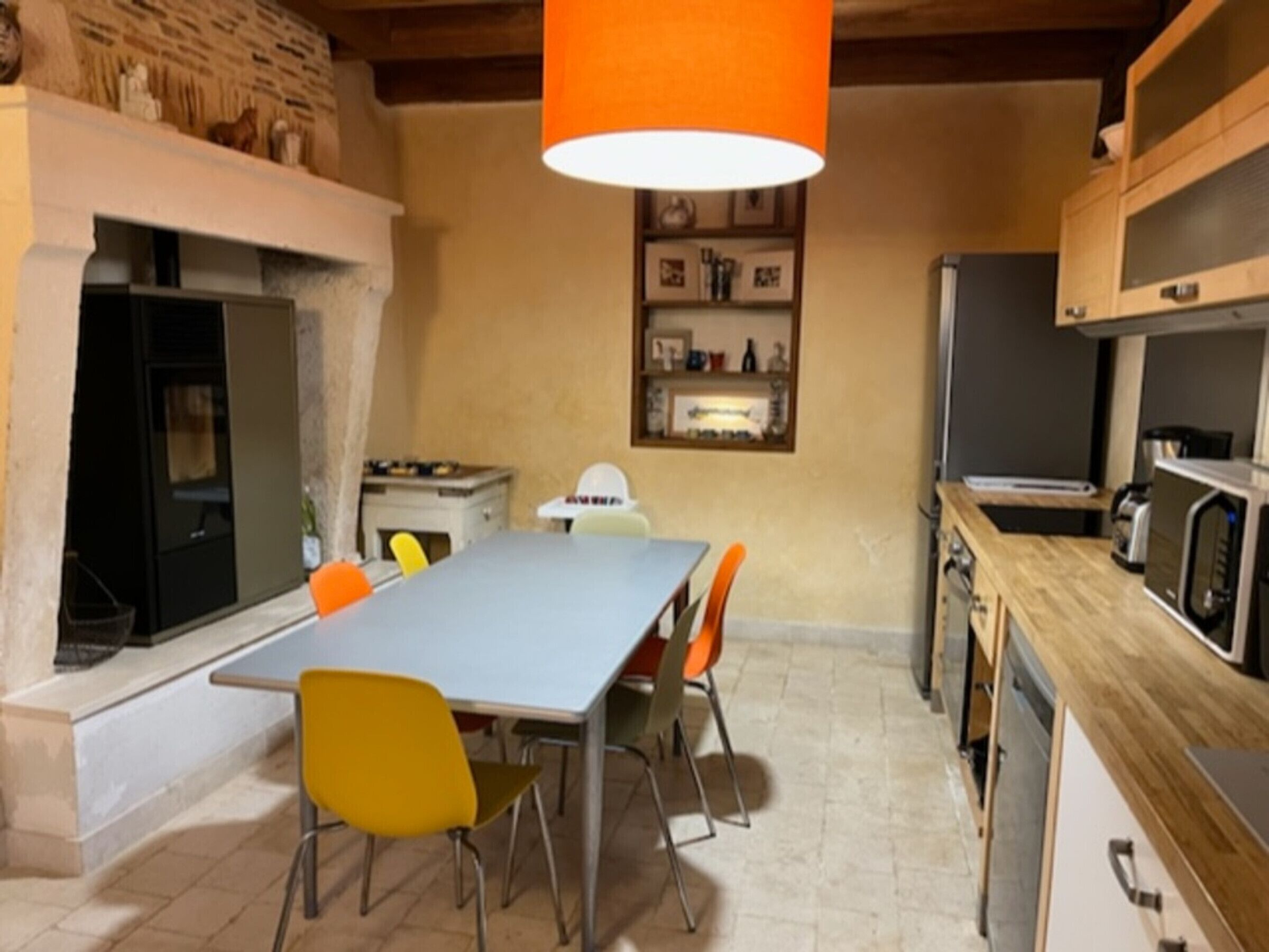 Une cuisine moderne avec un coin repas, comprenant une grande table, des chaises et un luminaire orange suspendu.