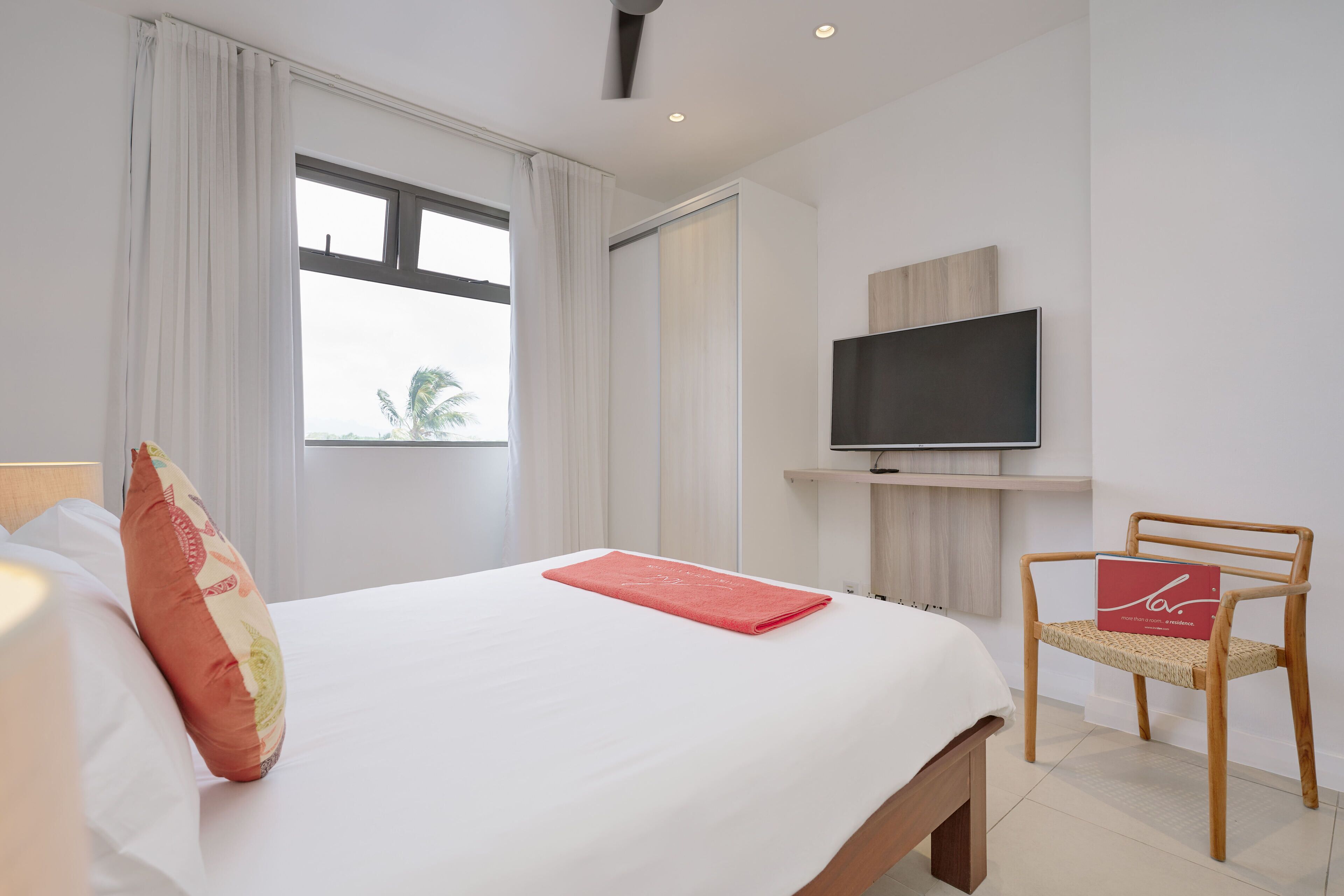 Een hotelkamer met een groot bed, een aan de muur bevestigde televisie, een stoel en een raam met gordijnen.