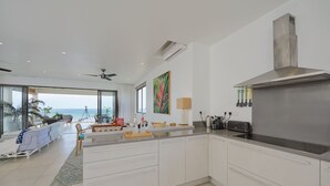 A modern kitchen with white cabinetry, a stainless steel range hood, and a large island. - Otera 2 Residence (Trou aux Biches)