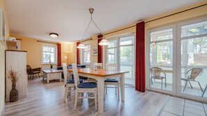 Un comedor amplio con una mesa y sillas de madera, ventanas grandes con cortinas rojas y vistas al exterior.