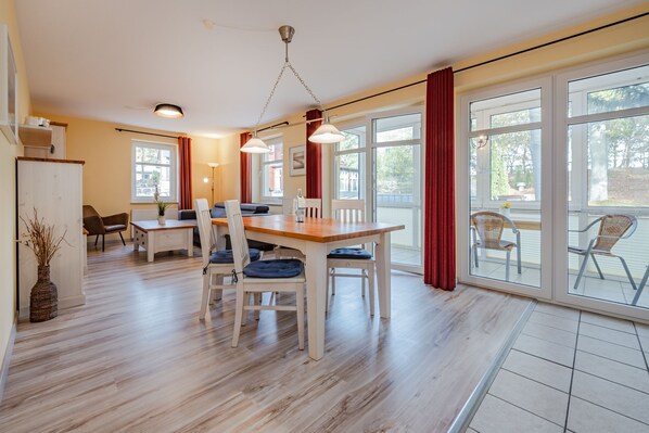 Een ruime eetruimte met een houten tafel en stoelen, grote ramen met rode gordijnen en uitzicht op de omgeving.