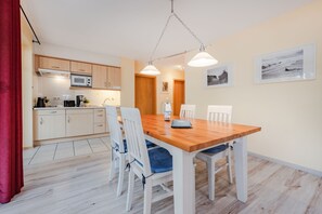 Ett modernt kök med träskåp, en mikrovågsugn och en matplats med ett träbord och vita stolar.